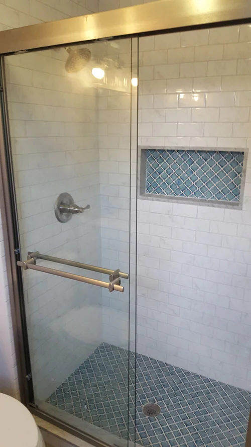Walk-in shower with white subway tile, mosaic niche and glass door
