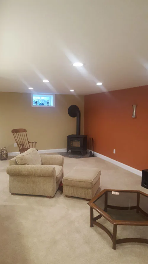 Finished basement living area with a wood stove and accent wall