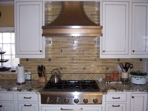 Kitchen range wall with a copper hood, mosaic backsplash and white cabinets
