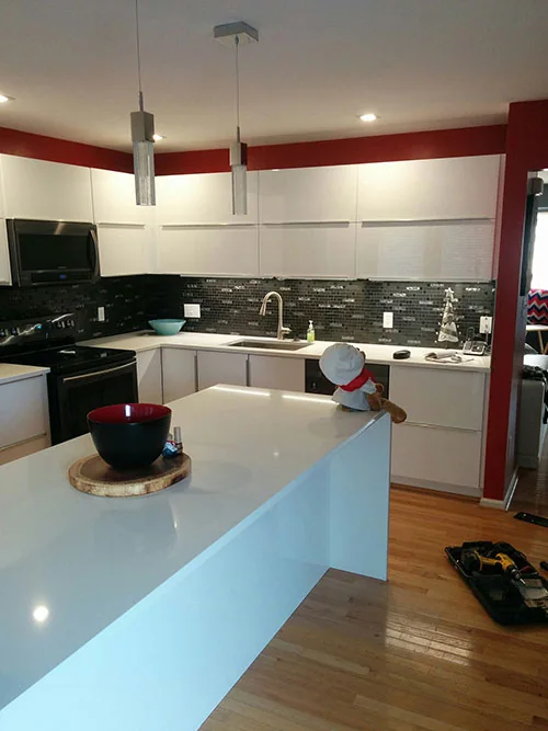 Modern kitchen with white waterfall island, black mosaic backsplash and pendant lighting