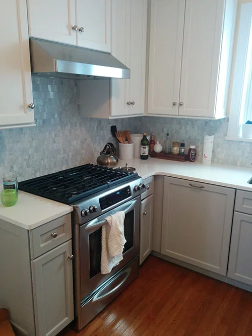 L-shaped kitchen with white cabinets, glass mosaic backsplash and gas range
