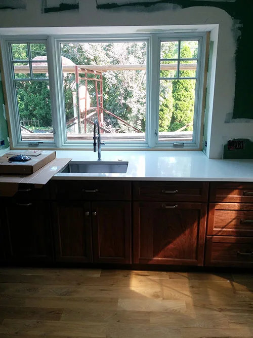Kitchen sink wall with new cherry cabinets and white counters under a large window